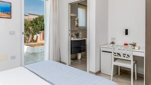 A bedroom with a bed, a desk, and a chair. There is a bathroom visible through an open door. - Villa I Chiani 8 Emma Villas (Gagliano del Capo)