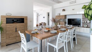 A modern kitchen with a wooden dining table set for six, white chairs, and a built-in TV. - Villa I Chiani 8 Emma Villas (Gagliano del Capo)