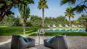 Zona junto a la piscina con sillones reclinables, una mesa con una botella y vasos, y vistas a la piscina y zonas verdes.