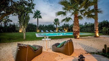 Un espace aménagé au bord de la piscine, comprenant une piscine, des chaises longues et une table avec une bouteille et un verre.