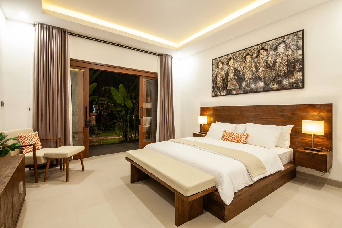 A modern hotel room with a large bed, a bench, a desk, and a view of the outdoors.
