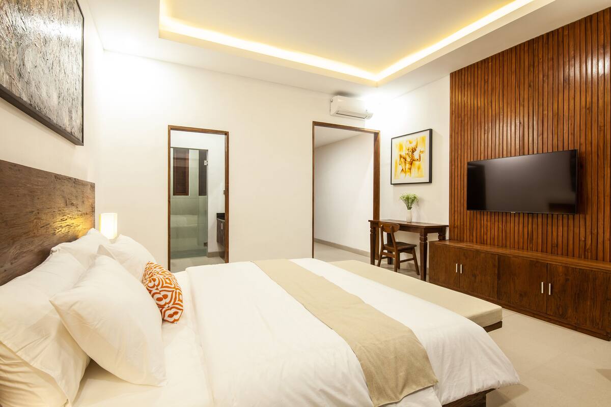 A modern hotel room with a large bed, wooden paneling, a flat-screen TV, and a desk with a chair.