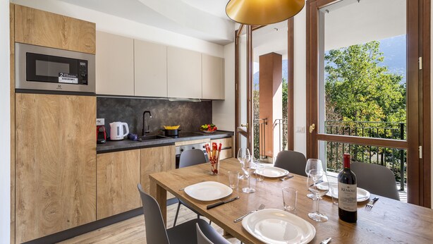 A modern kitchen with a microwave, wooden cabinets, and a dining area set for a meal. - Porto Letizia Rossini 9, Porlezza, Italy (Porlezza)