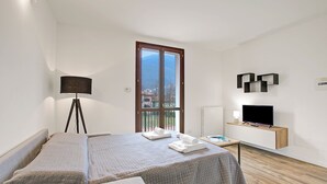 A hotel room with a bed, a desk, a television, a lamp, and a window with a view of buildings. - Porto Letizia Rossini 9, Porlezza, Italy (Porlezza)