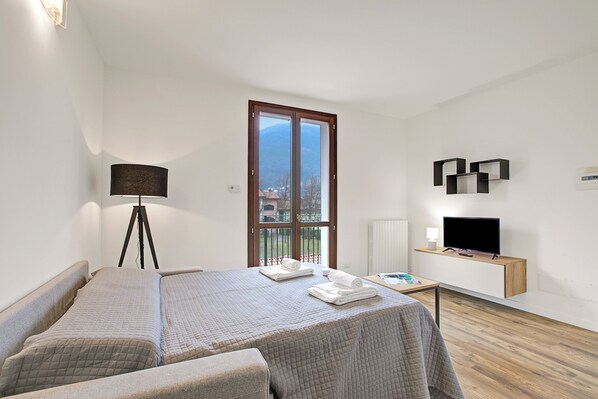 Ein Hotelzimmer mit Bett, Schreibtisch, Fernseher, Lampe und einem Fenster mit Blick auf Gebäude.