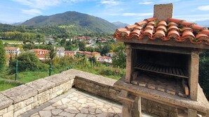 A stone barbecue grill with a tiled roof, set against a backdrop of a mountainous landscape and a village. - La Rectoral Arriondas (Arriondas)