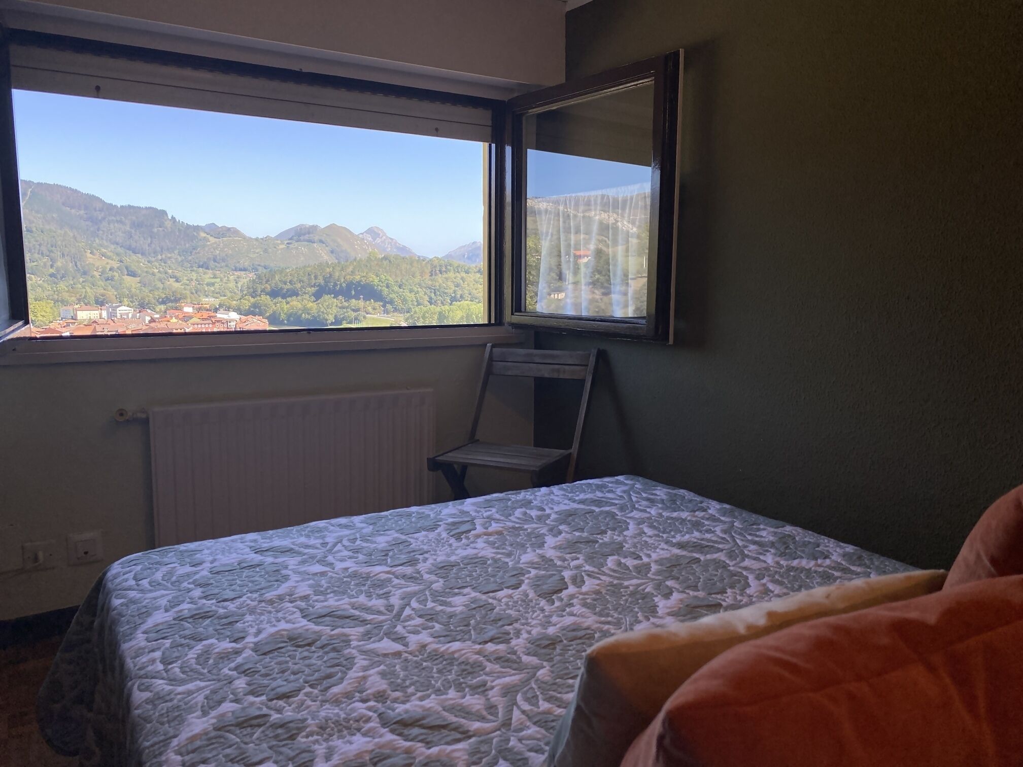 Een slaapkamer met een bed, een raam met uitzicht op bergen, een radiator en een stoel.