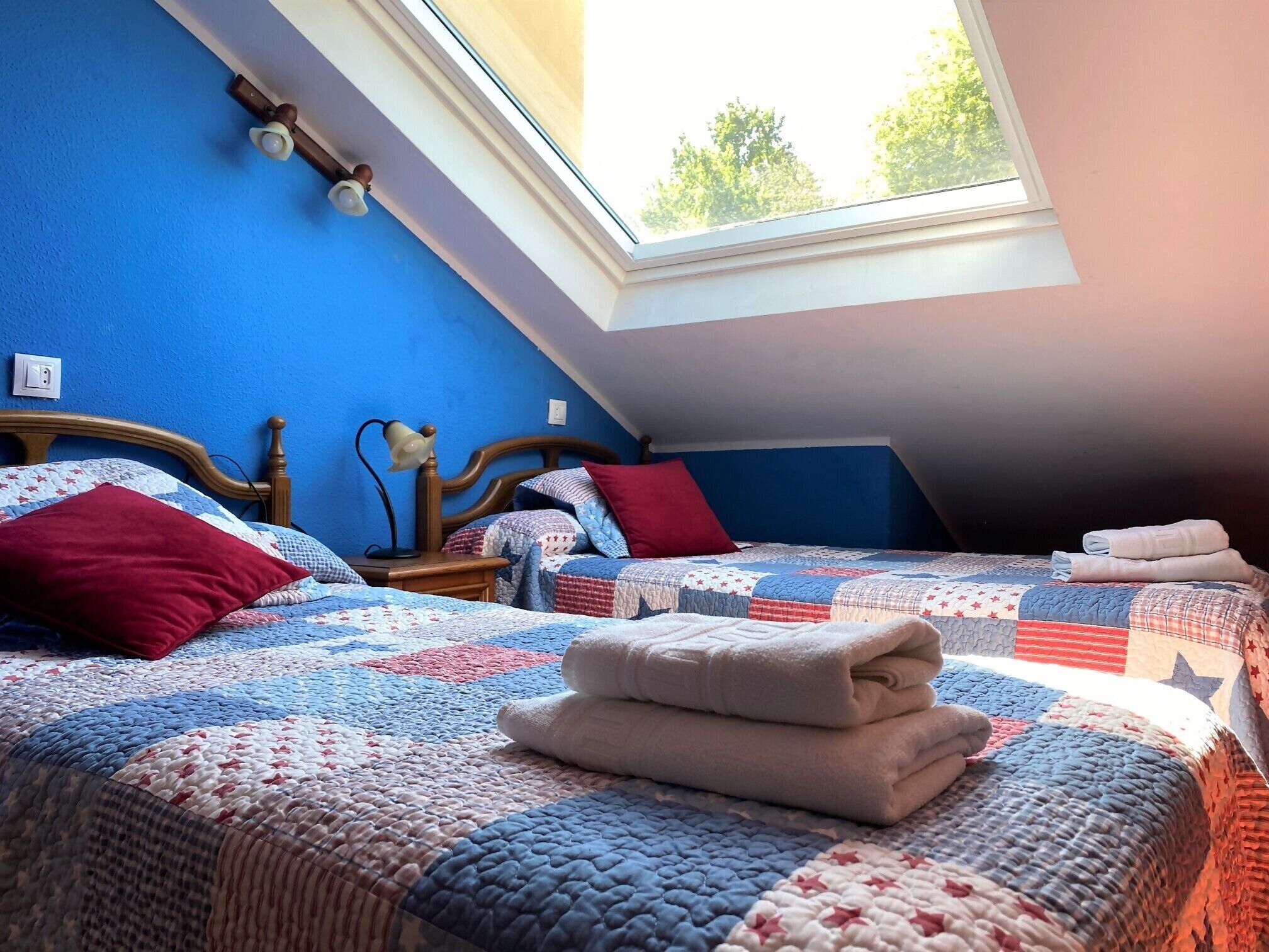 A bedroom with two beds, a skylight, and a wooden headboard.