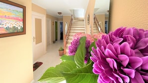 A hallway with a staircase, a framed painting, and a potted plant with purple flowers. - La Rectoral Arriondas (Arriondas)