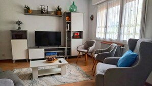 A modern living room with a flat-screen TV, grey armchairs, a white coffee table, and a bookshelf with decorative items. - La Rectoral Arriondas 2 (Arriondas)