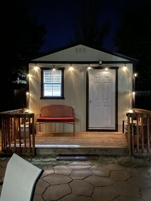 A small, wooden shed with a door and a window, illuminated by string lights. - The Little House - Eclectic, Quiet, Pet Friendly Home (Amarillo)