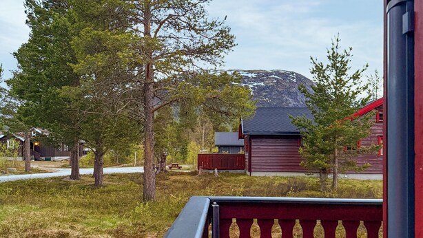 A rustic cabin with a red roof, surrounded by trees and a mountain in the background.
