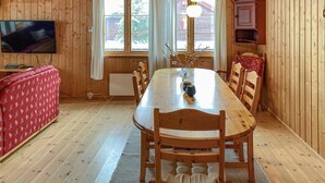 A wooden-paneled room with a dining table, chairs, a television, and a window with curtains.