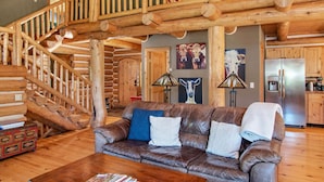 L’intérieur d’une cabane en rondins, avec un escalier en bois, un canapé en cuir et un coin cuisine.
