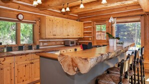 Une cuisine de style rustique, aménagée comme une cabane, avec des meubles en bois, un grand îlot central doté d’un bord en bois naturel et un coin bar avec des tabourets.