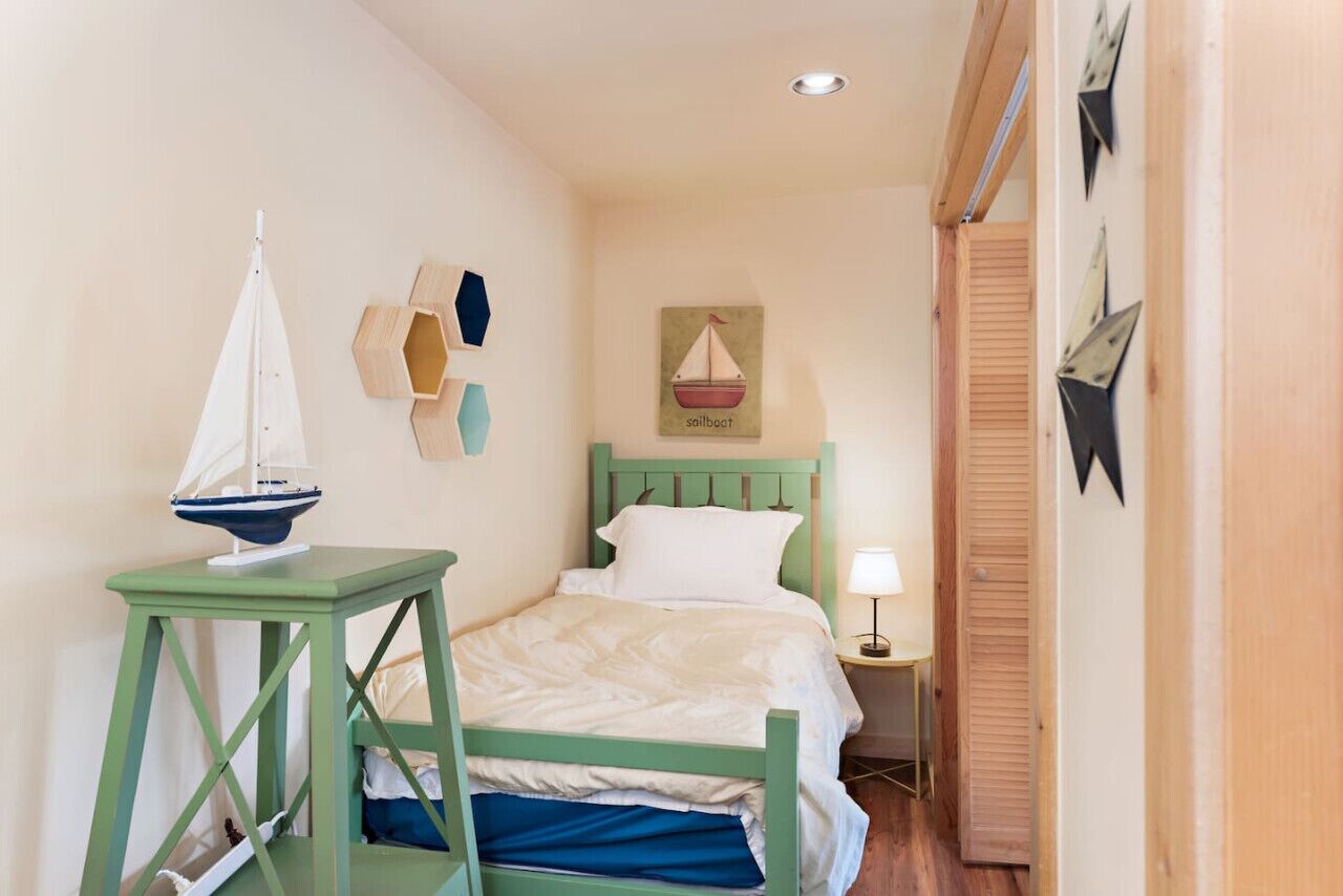 Une petite chambre à coucher accueillante, avec un lit simple, une table de chevet, une décoration murale représentant un voilier et une petite table avec une lampe.