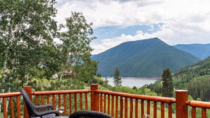 Une terrasse dotée de chaises et d’une table en osier, offrant une vue sur un lac et des montagnes.