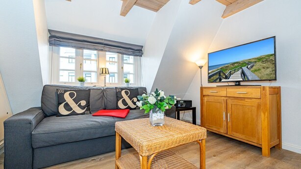 A cozy living room with a grey sofa, a wicker coffee table, and a wooden cabinet.