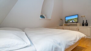 A bedroom with a large bed, a television on a stand, a small shelf, and two bottles on the dresser.