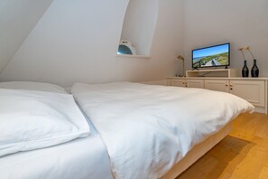 Ein Schlafzimmer mit einem großen Bett, einem Fernseher auf einem Schrank, einer kleinen Ablagefläche und zwei Flaschen auf dem Schminktisch.