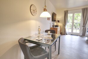 Ein Essbereich mit Glastisch, Stühlen, einer Uhr, einer Lampe und Blick durch eine Tür.