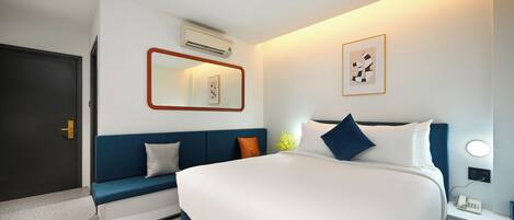 Una habitación de hotel moderna con una cama grande, un sofá azul, una mesita de noche con un teléfono y un equipo de aire acondicionado en la pared.