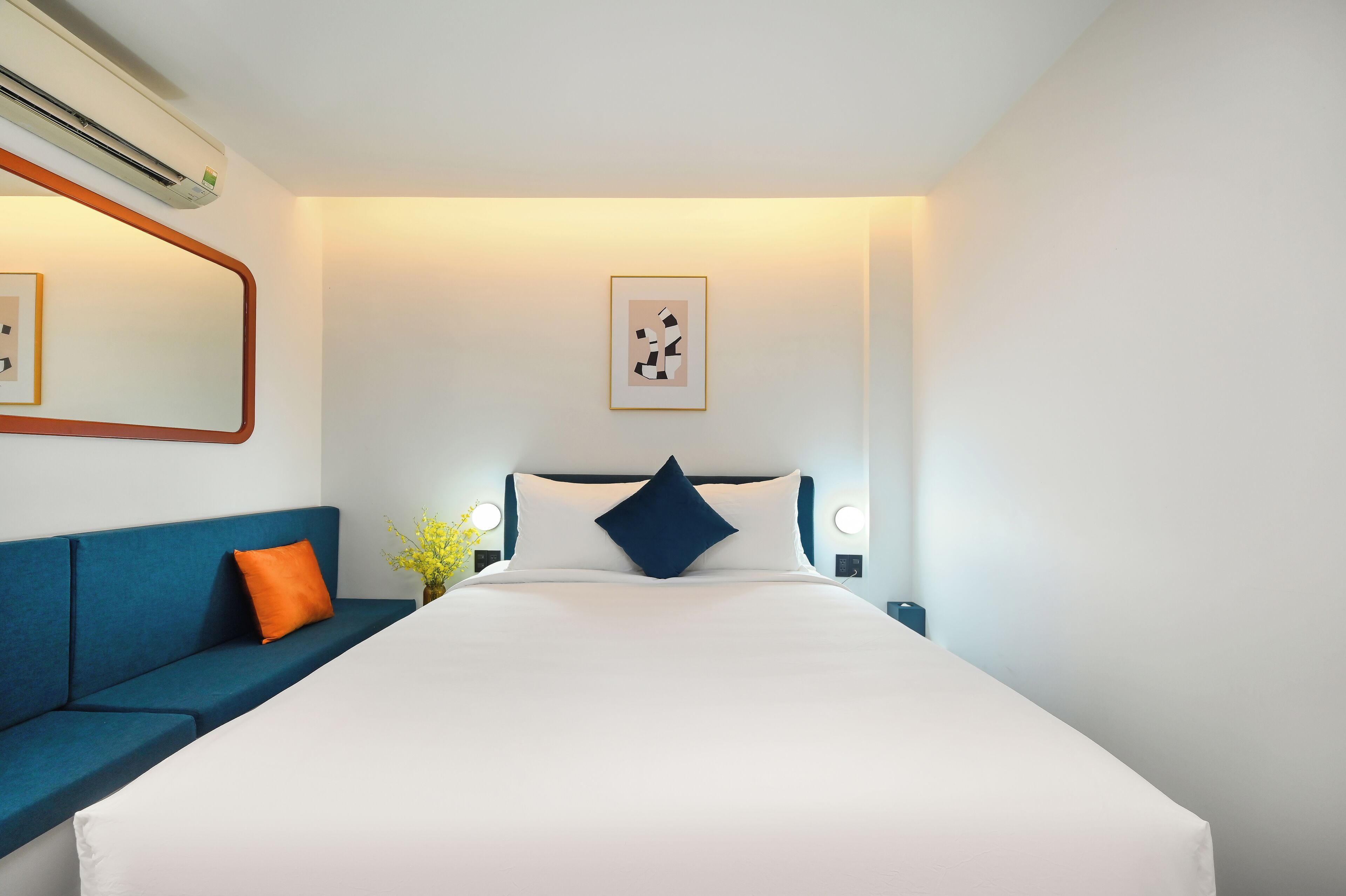 A modern hotel room with a large bed, a blue sofa, and a wall-mounted air conditioner.