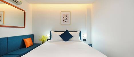 A modern hotel room with a large bed, a blue sofa, and a wall-mounted air conditioner.