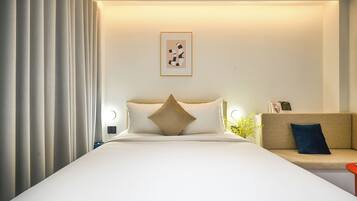 A hotel room with a bed, a sofa, a wall-mounted light, and a framed picture.