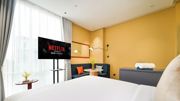 Une chambre d’hôtel avec un grand lit, un téléviseur posé sur un meuble, un canapé, une petite table avec un vase et un miroir fixé au mur.