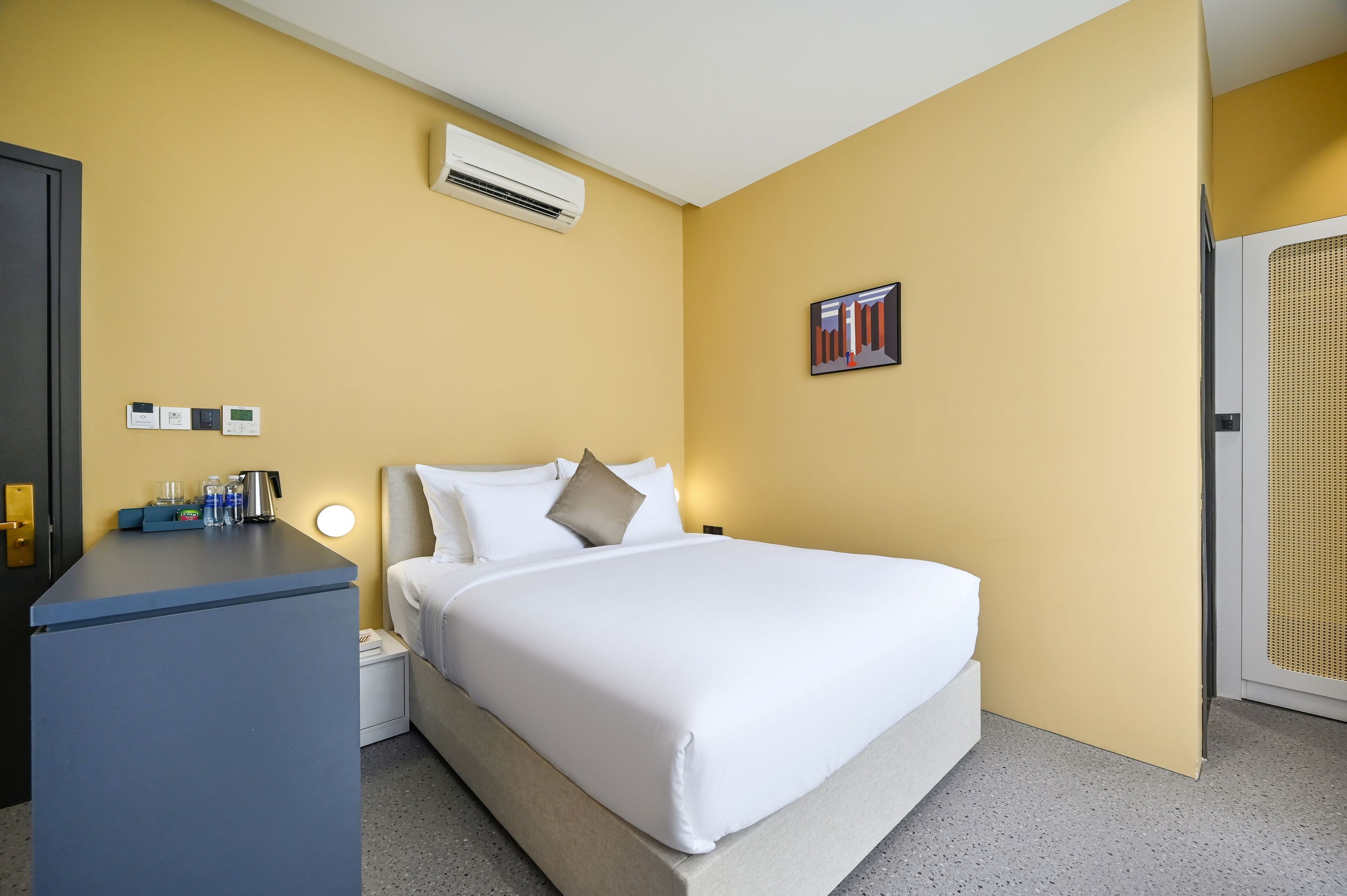 A hotel room with a bed, bedside table, and an air conditioning unit.