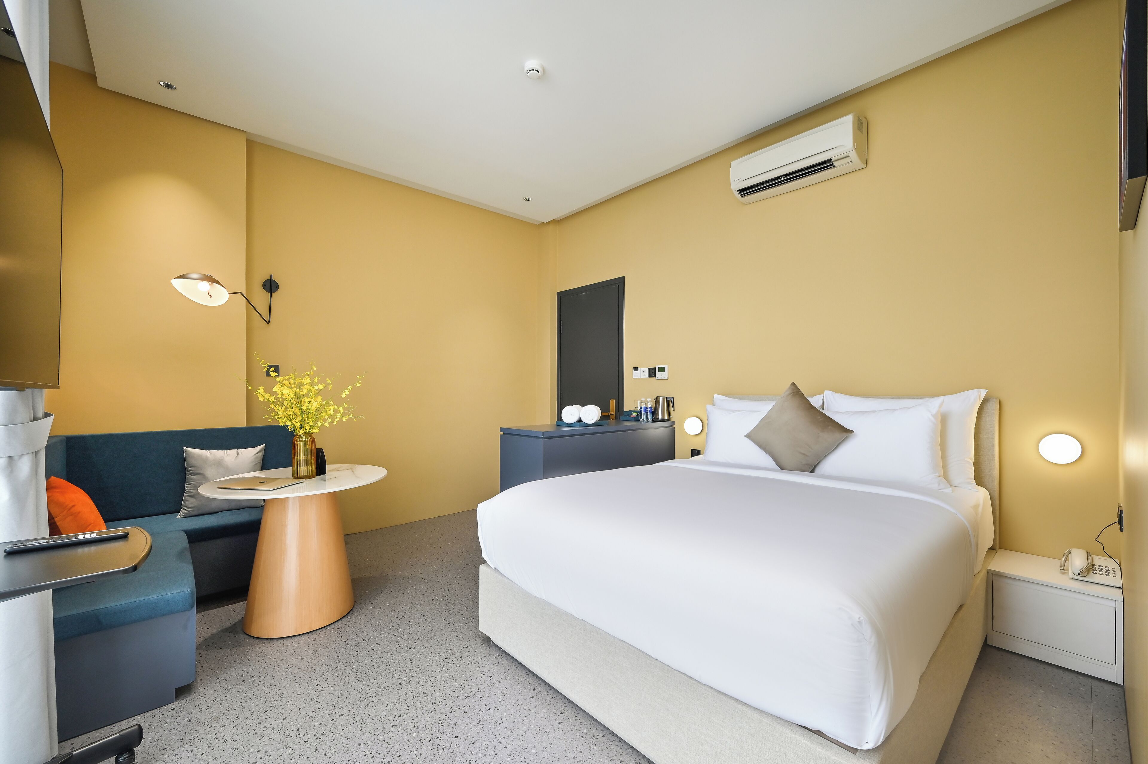 A modern hotel room with a large bed, a sofa, a small table, and a desk.