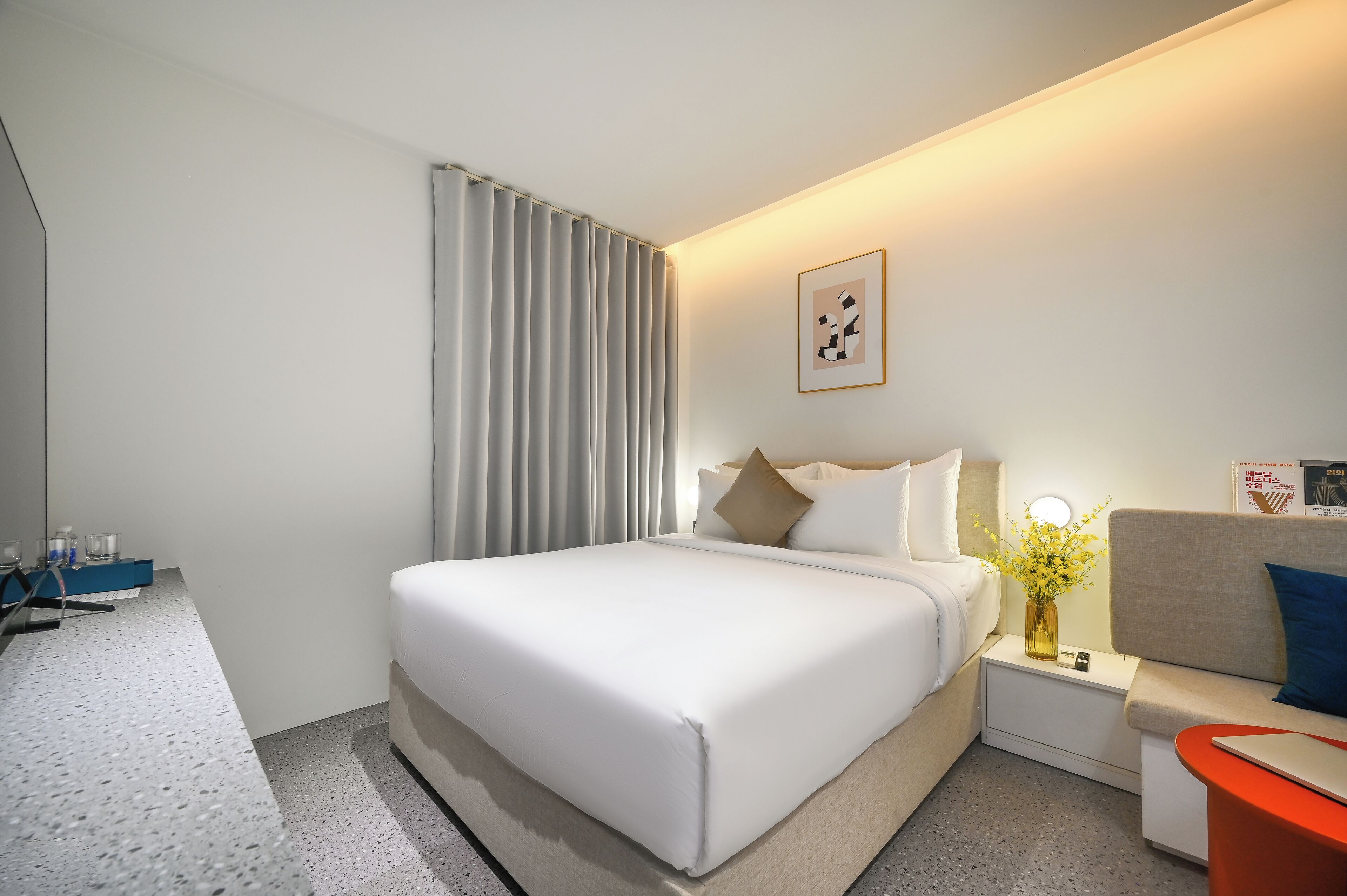 A hotel room with a large bed, bedside tables, a sofa, and a small table with a vase.