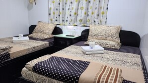 A hotel room with two beds, each with patterned bedding and pillows, a bedside table with a remote control, and a curtain with a floral design. - Bohol Hostel (Kowloon)