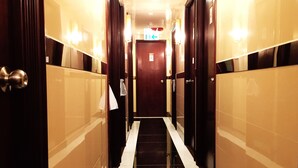 A hotel hallway with a dark wooden door marked 1007, a lighted exit sign, and a tiled floor. - Bohol Hostel (Kowloon)