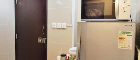 A hotel room with a dark wooden door, an exit sign, a refrigerator with an energy label, and a microwave on top.