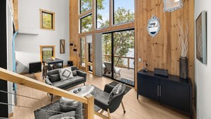 A spacious living area with a wooden interior, large windows, a sofa set, and a staircase. - Black Diamond: "Waterfront Finger Lakes Home with Hot Tub!" (Hector)