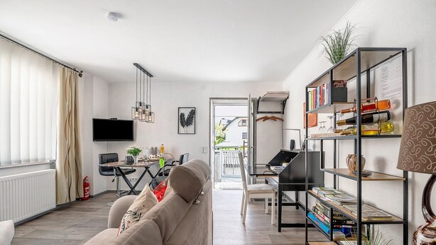 En moderne stue med sofa, fjernsyn, spiseområde og reol.