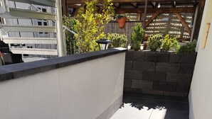 En tagterrasse med mørke fliset gulv, hvid væg og en pergola i træ.