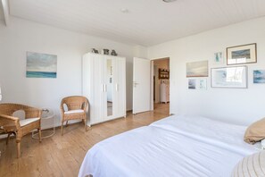 A bedroom with a large bed, two wicker chairs, a wardrobe, and a door leading to another room. - Hygge Frisian House by the Sea with Private Garden and Terrace (Nordstrand)