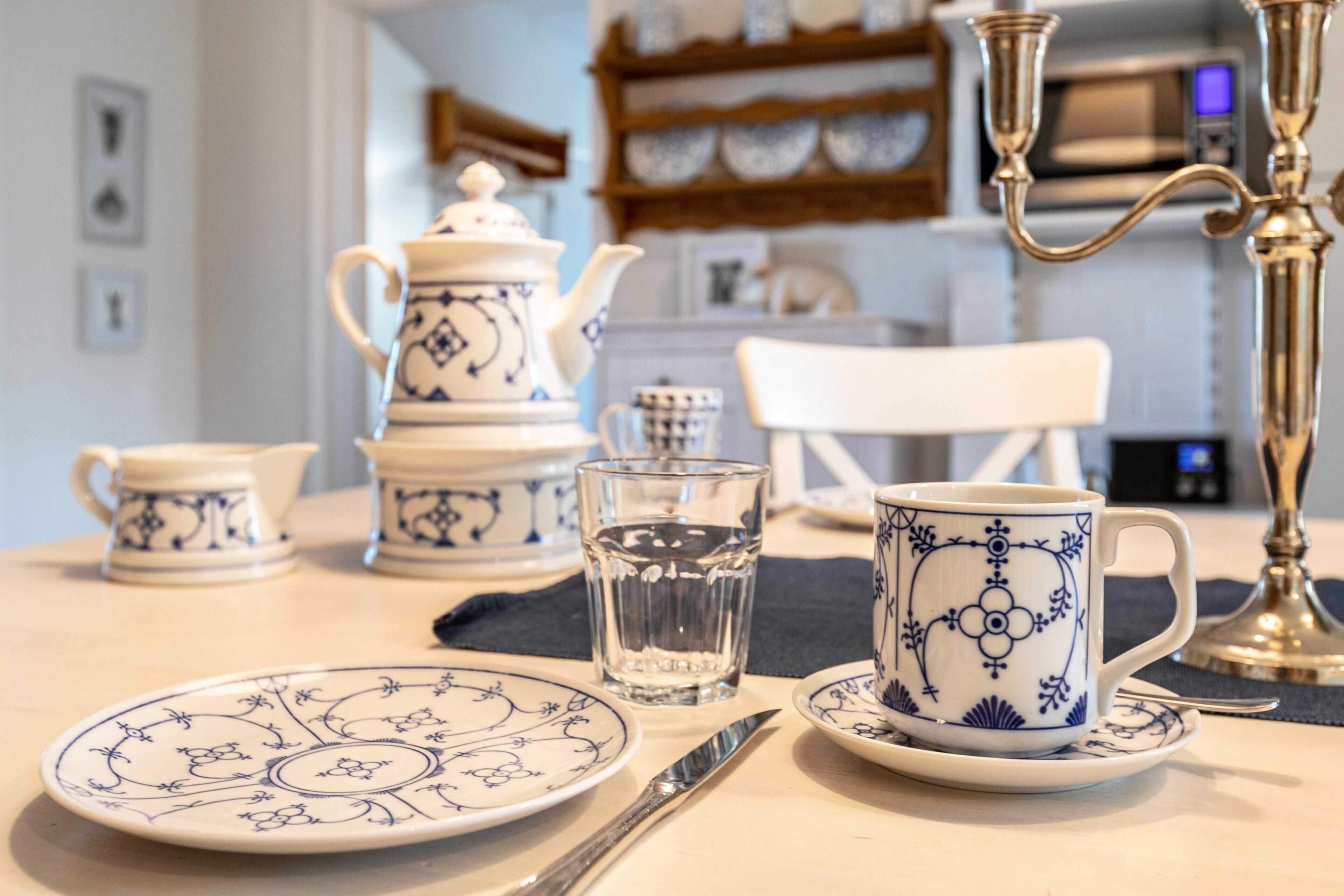 A table set with a teapot, cups, a glass, and a knife.
