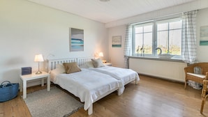 Un dormitorio con dos camas, una ventana con cortinas, un radiador y una silla de mimbre.