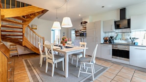 Una cocina moderna con armarios blancos, una escalera de madera y un comedor con sillas y mesa blancos.