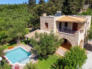 Une villa en pierre dotée d’une piscine, d’un balcon et offrant une vue sur la verdure environnante.