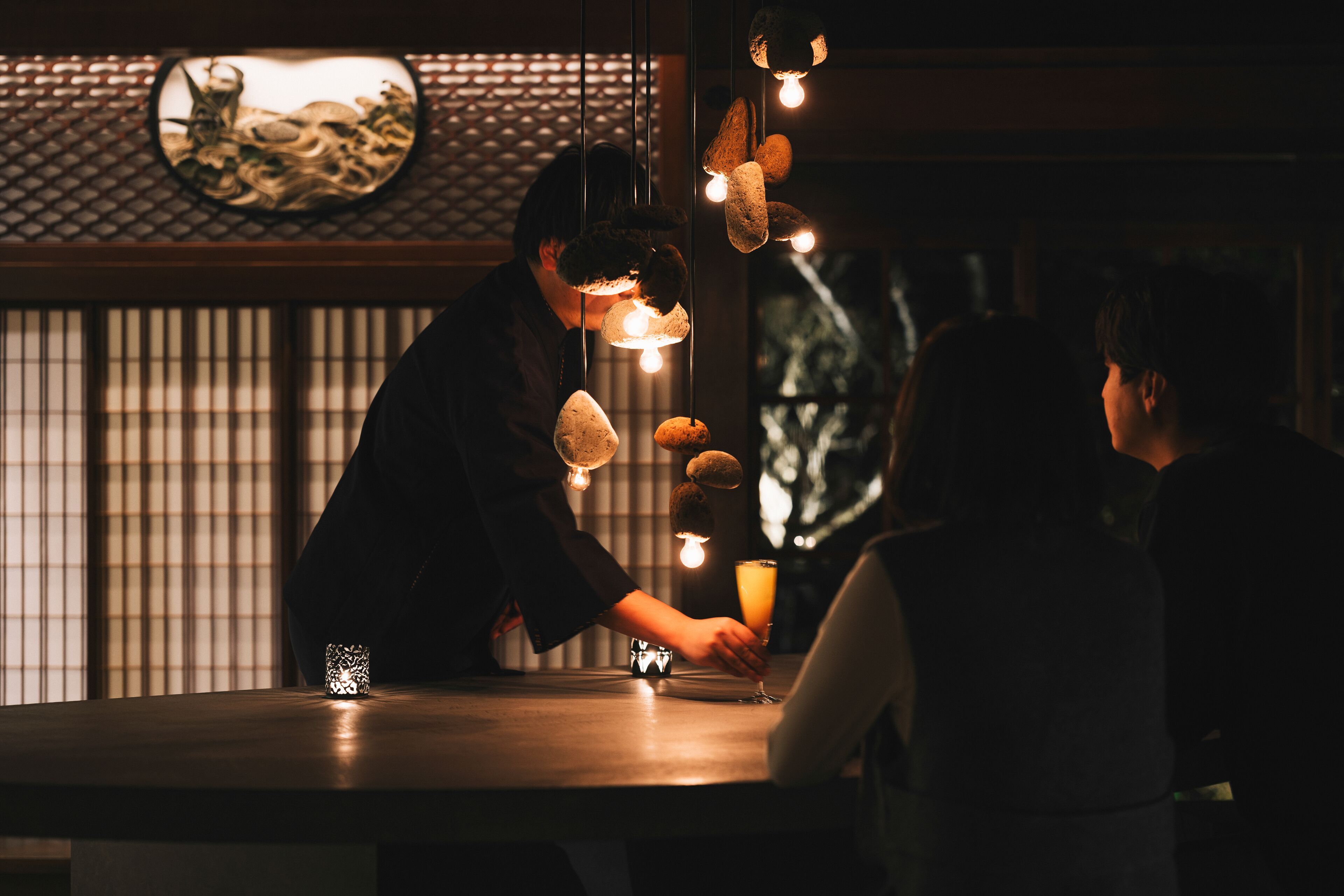 Uma pessoa servindo uma bebida em um bar com decoração tradicional e luminárias pendentes.