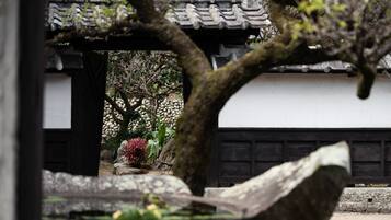 A traditional Japanese building with a tiled roof, a stone pathway, and a garden with rocks and plants.