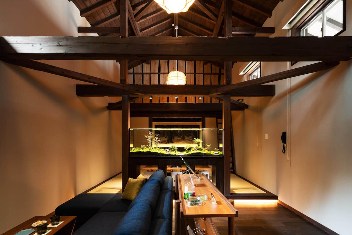 A cozy room with a wooden ceiling, a large fish tank, a sofa, and a table with various items.