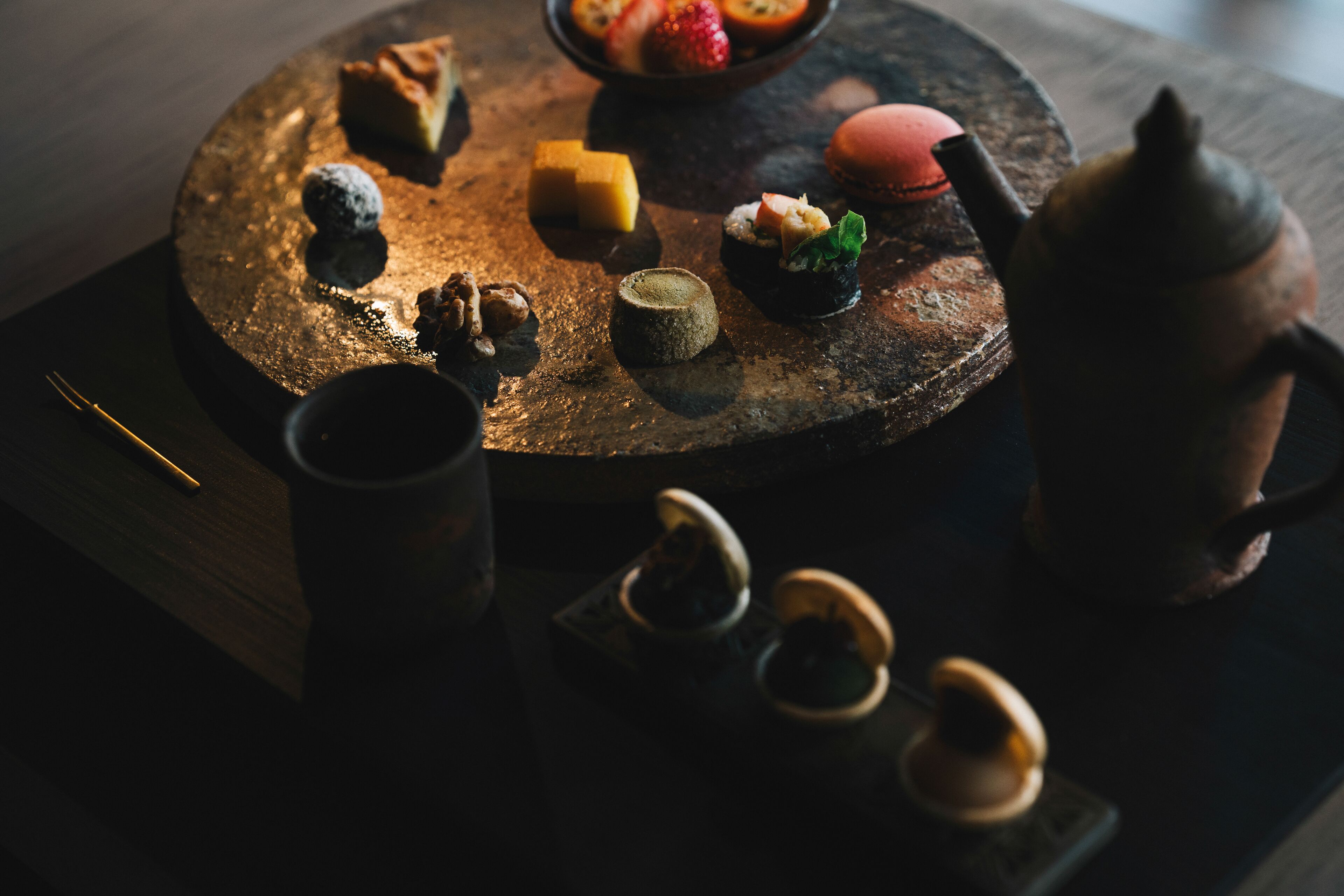 A round wooden table with various food items and a teapot.