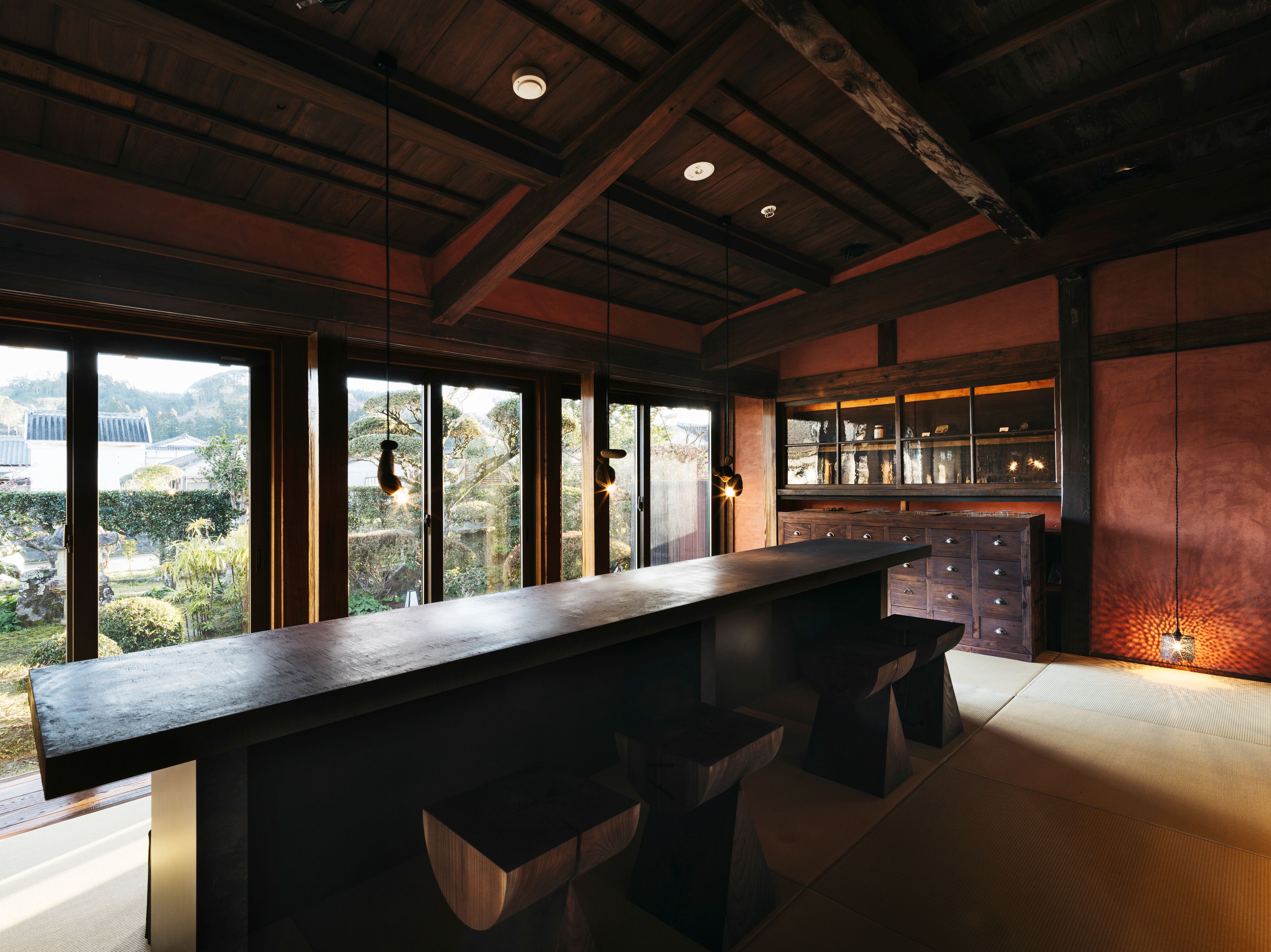 A modern kitchen with a long counter, wooden cabinets, and large windows offering a view of the surrounding landscape.