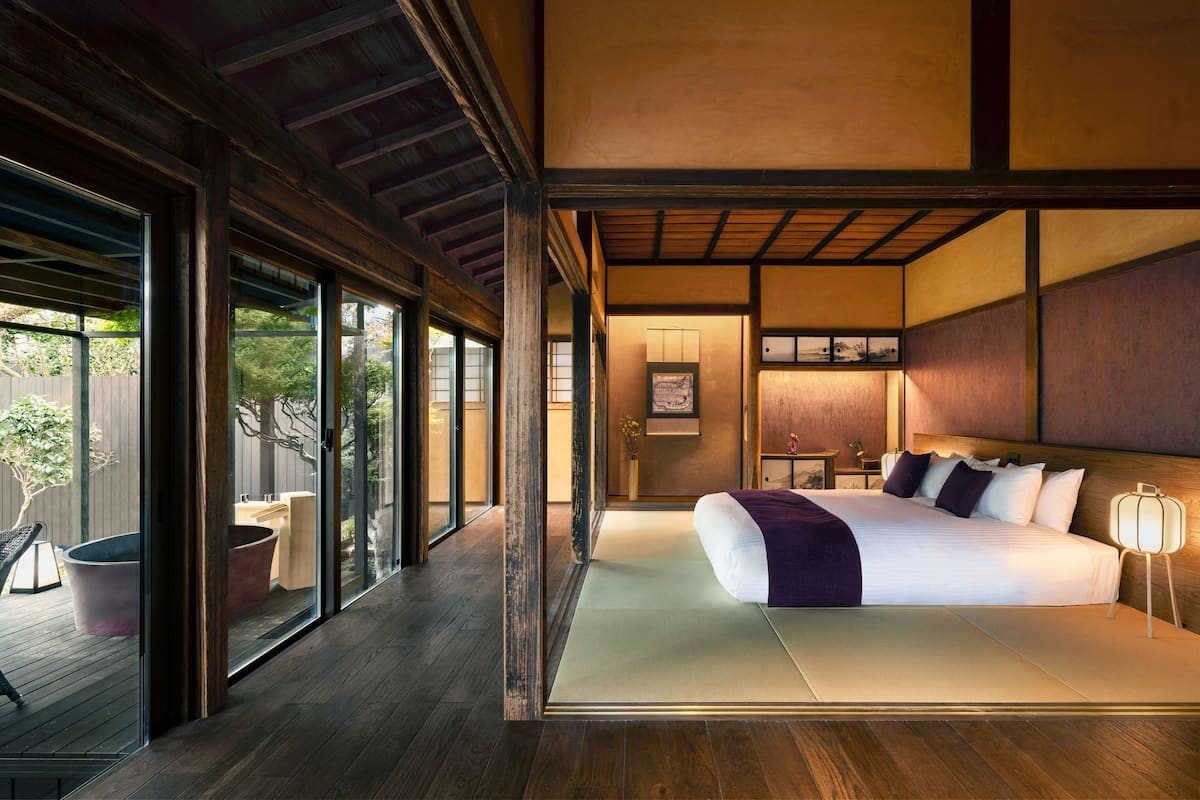 A modern bedroom with a large bed, sliding glass doors leading to a deck, and a traditional Japanese-style interior.